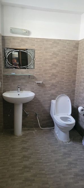 A bathroom with a pedestal sink, a toilet, and a mirror with a decorative frame.