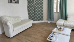 Sala de estar com sofá branco, mesa de centro branca com revistas, parede estampada e janela com cortinas.