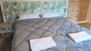 Ein Schlafzimmer mit Stehwänden, einem Bett mit gestepptem Kopfteil, zwei Nachttischen und einem Beistelltisch mit Lampe.