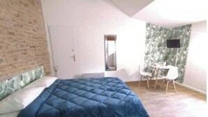 Ein Schlafzimmer mit einem großen Bett, einem kleinen Tisch und einem Stuhl. Im Raum befindet sich eine Tür und ein Fenster.