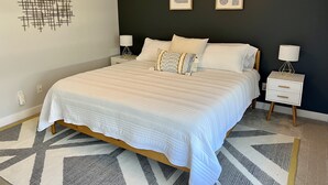 A modern bedroom with a large bed, two bedside tables, and a geometric wall decoration. - Pristine Condo, Close to Downtown, Beaches, GT Commons, and Restaurants (Traverse City)