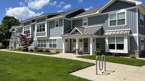 A two-story residential building with a covered front porch and a landscaped front yard. - Pristine Condo, Close to Downtown, Beaches, GT Commons, and Restaurants (Traverse City)