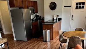 A modern kitchen with stainless steel appliances, wooden cabinets, and a dining area with orange chairs and a round table. - Pristine Condo, Close to Downtown, Beaches, GT Commons, and Restaurants (Traverse City)