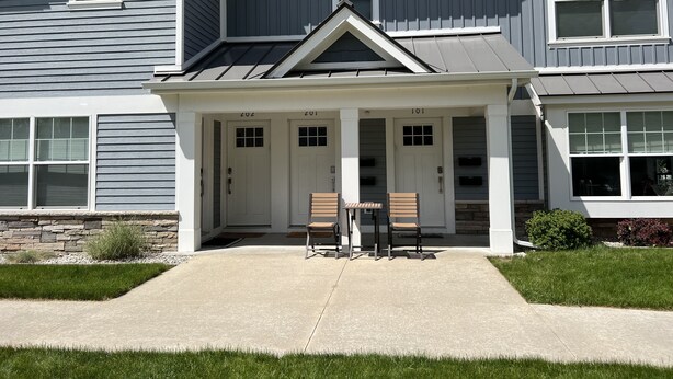 A two-story residential building with a covered porch, numbered doors, and a stone foundation. - Pristine Condo, Close to Downtown, Beaches, GT Commons, and Restaurants (Traverse City)