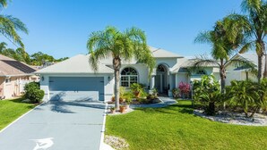 A single-story house with a garage, surrounded by well-maintained lawns and palm trees. - Dock Holliday by Ryson Vacation Rentals (Palm Coast)