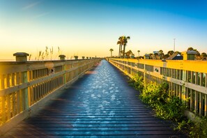 Un muelle de madera que lleva a una playa con palmeras y cabañas.