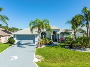 A single-story house with a garage, surrounded by well-maintained lawns and palm trees. - Dock Holliday by Ryson Vacation Rentals (Palm Coast)