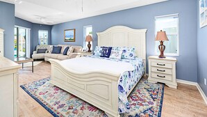 A bedroom with a large bed, a ceiling fan, a nightstand with a lamp, and a view of the outdoors through a sliding door. - Dock Holliday by Ryson Vacation Rentals (Palm Coast)
