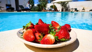 A bowl of strawberries on a table by a pool with lounge chairs and umbrellas in the background.