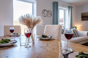 A dining table with plates of food and glasses of red wine, a vase with dried plants, and a view of the city through a window. - Alde Seagull, Aldeburgh (Aldeburgh)