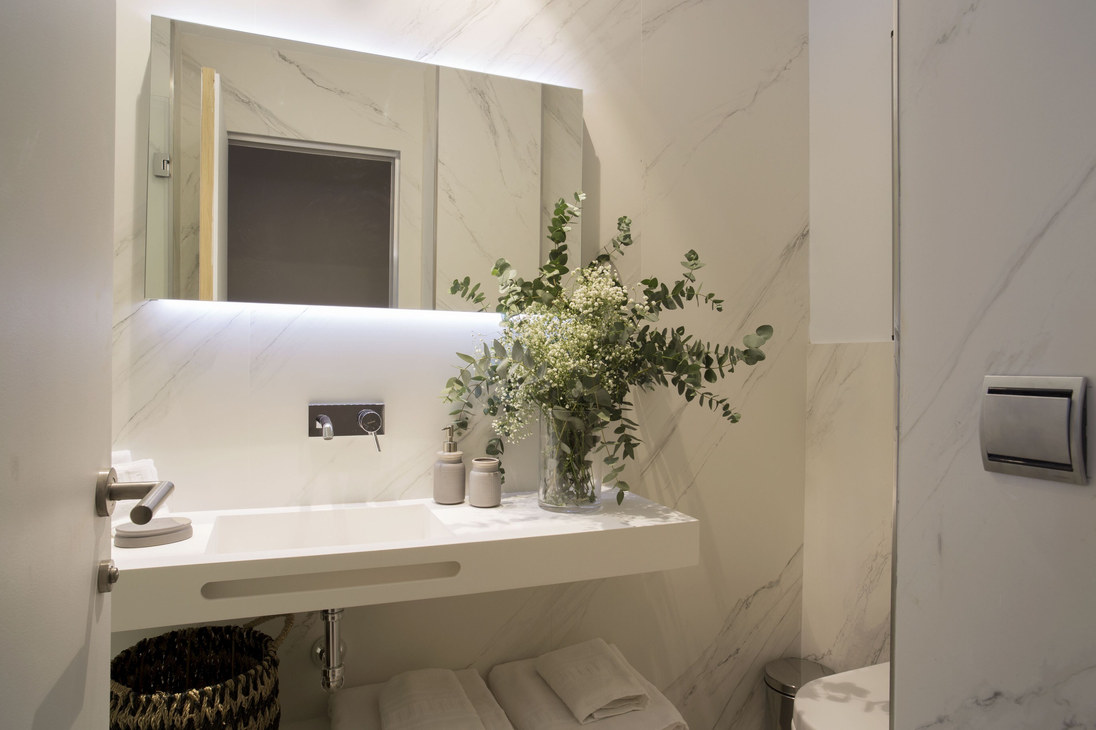 Ein modernes Badezimmer mit Marmorwaschtisch, einem Spiegel, einer Blumenvase und einem Handtuchhalter.