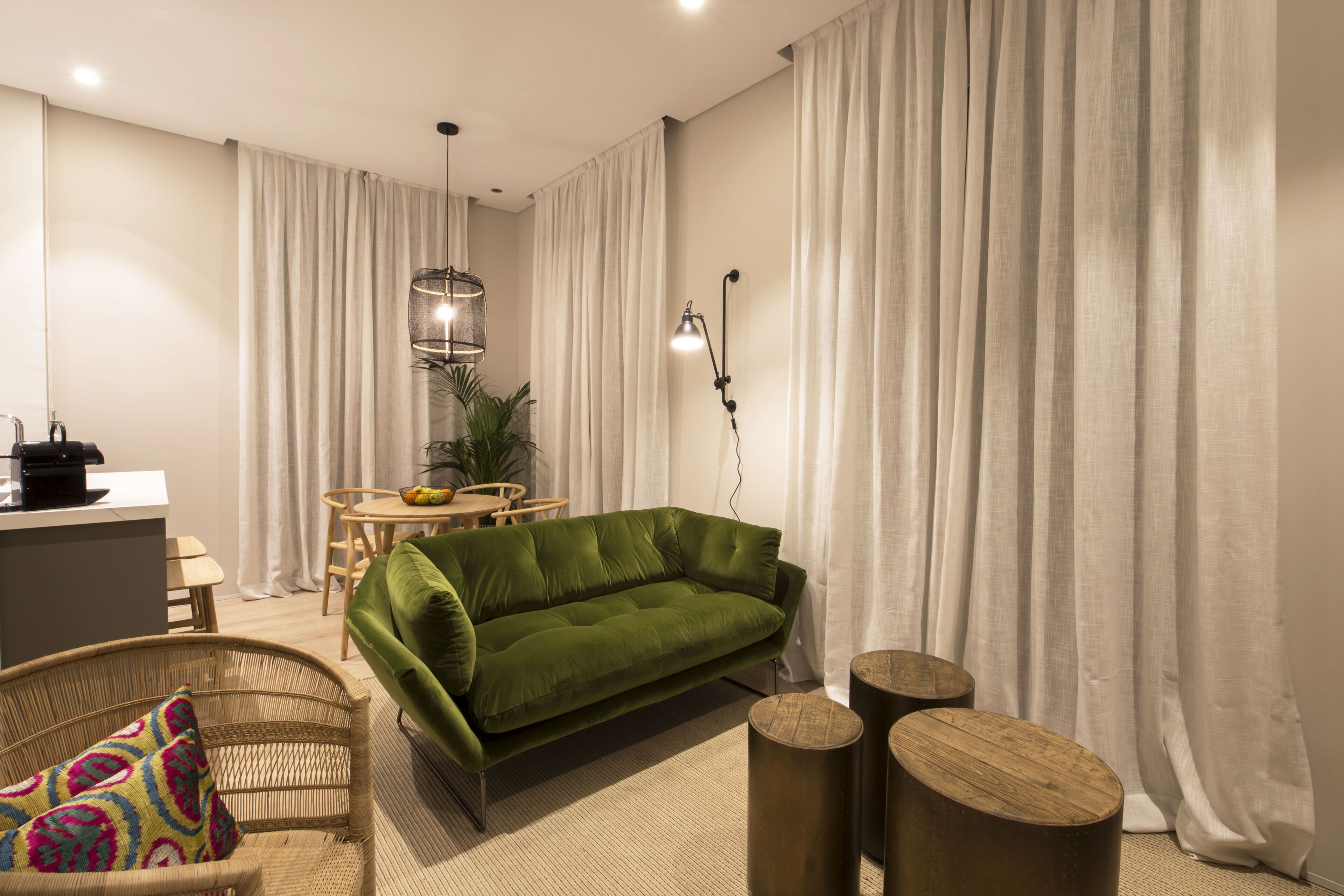 A modern living room with a green sofa, a wicker chair, a small round table, and a pendant light.