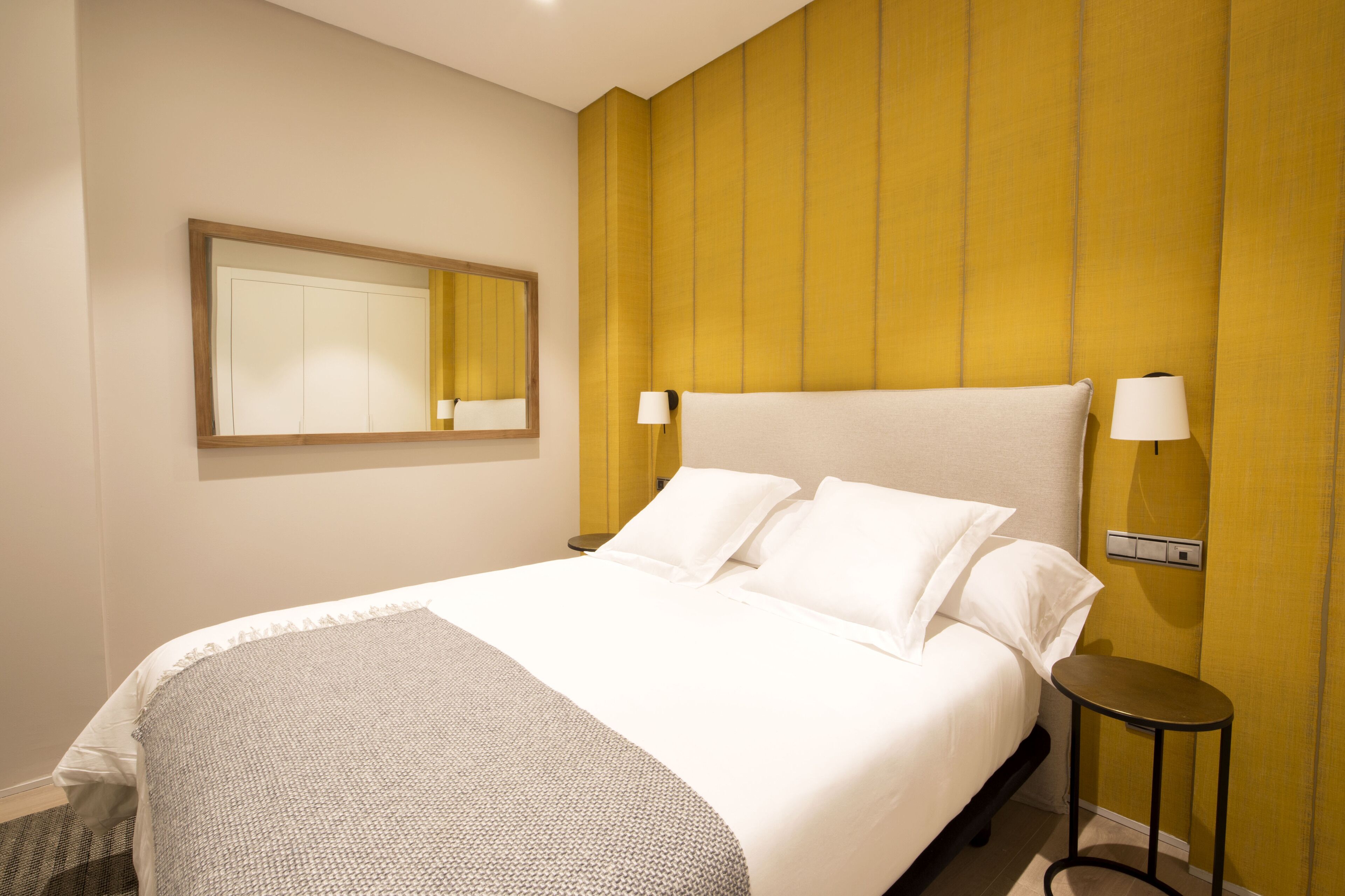 Una habitación de hotel con una cama grande, una mesita de noche, un espejo y una lámpara de pared.