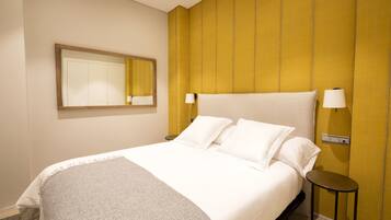 Una habitación de hotel con una cama grande, una mesita de noche, un espejo y una lámpara de pared.
