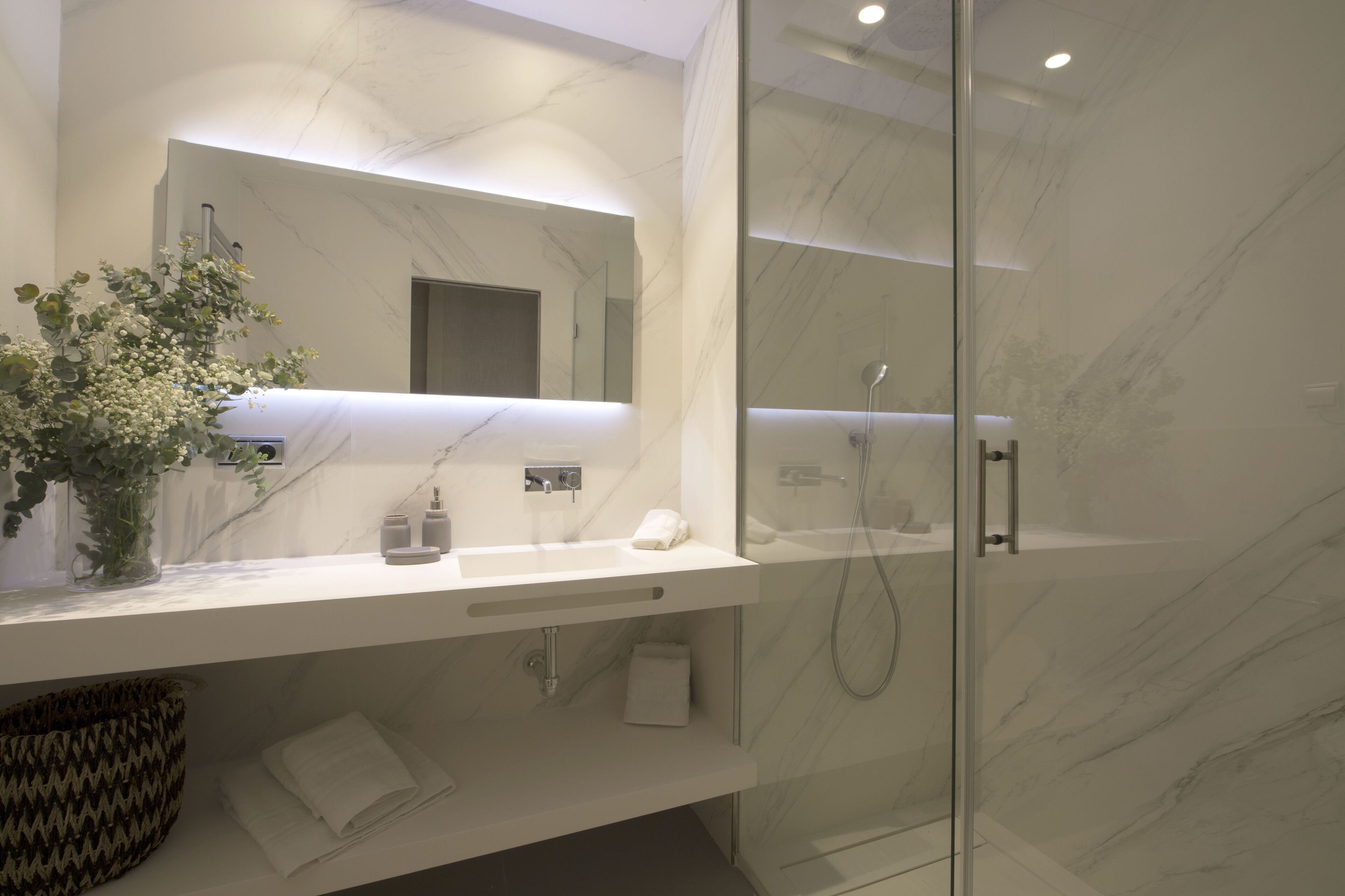 A modern bathroom with a marble countertop, a glass shower enclosure, and a vase with flowers.