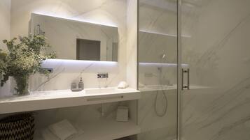 A modern bathroom with a marble countertop, a glass shower enclosure, and a vase with flowers.