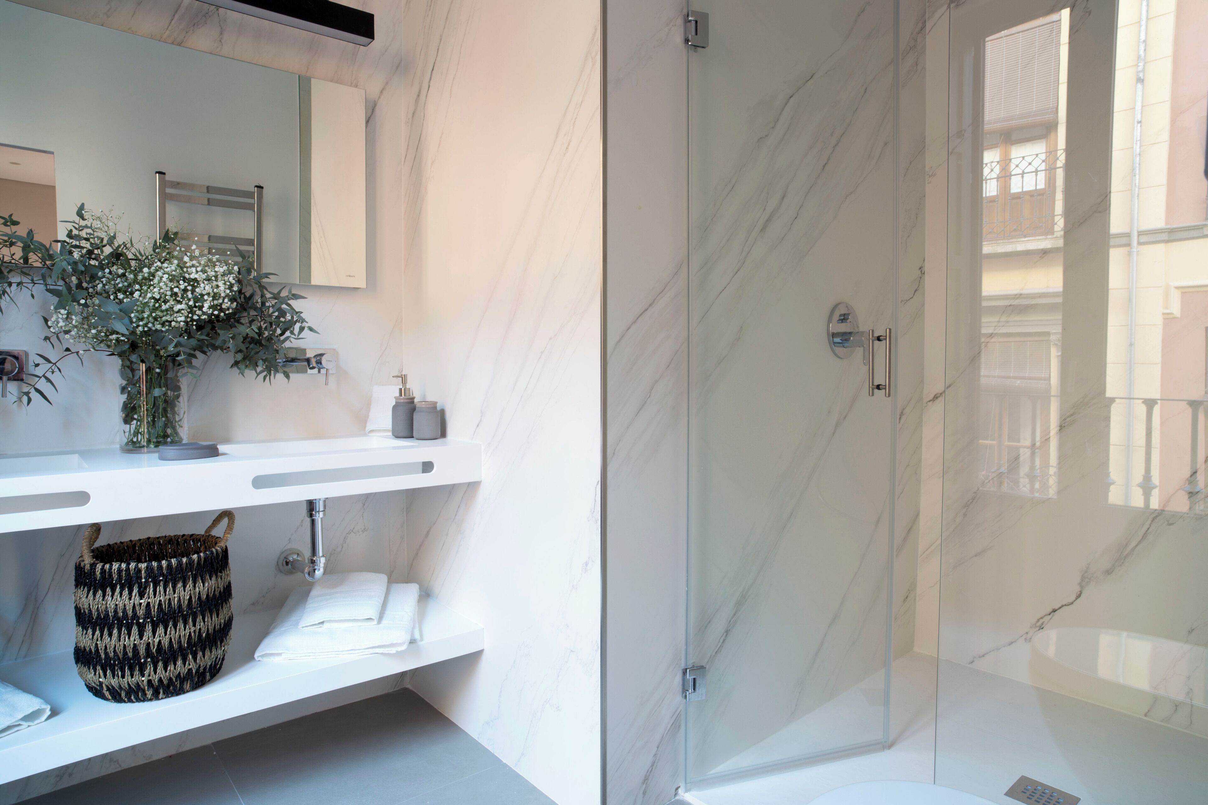 Un baño moderno con cabina de ducha de vidrio, encimera de mármol y un espejo grande.