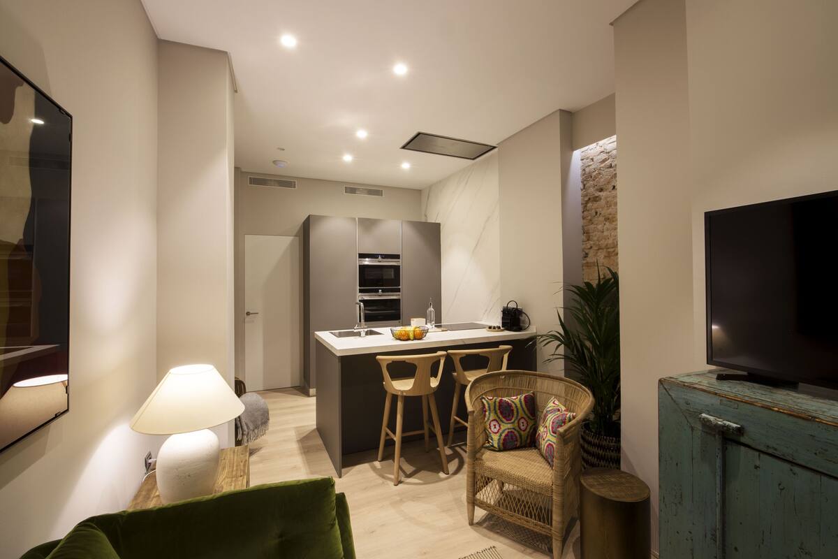 A compact living space with a kitchenette, a dining area with bar stools, a television, and a green sofa.