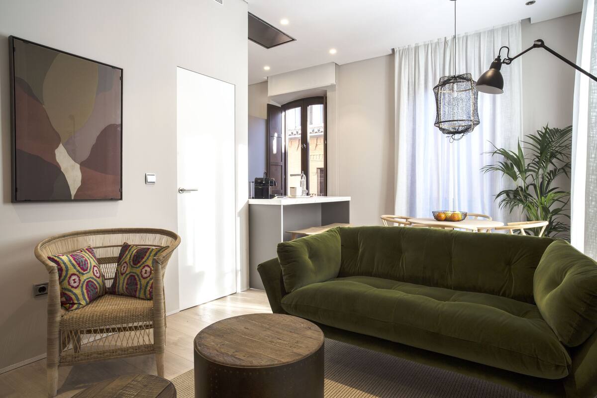 A modern living room with a green sofa, wicker chair, and a round wooden coffee table.