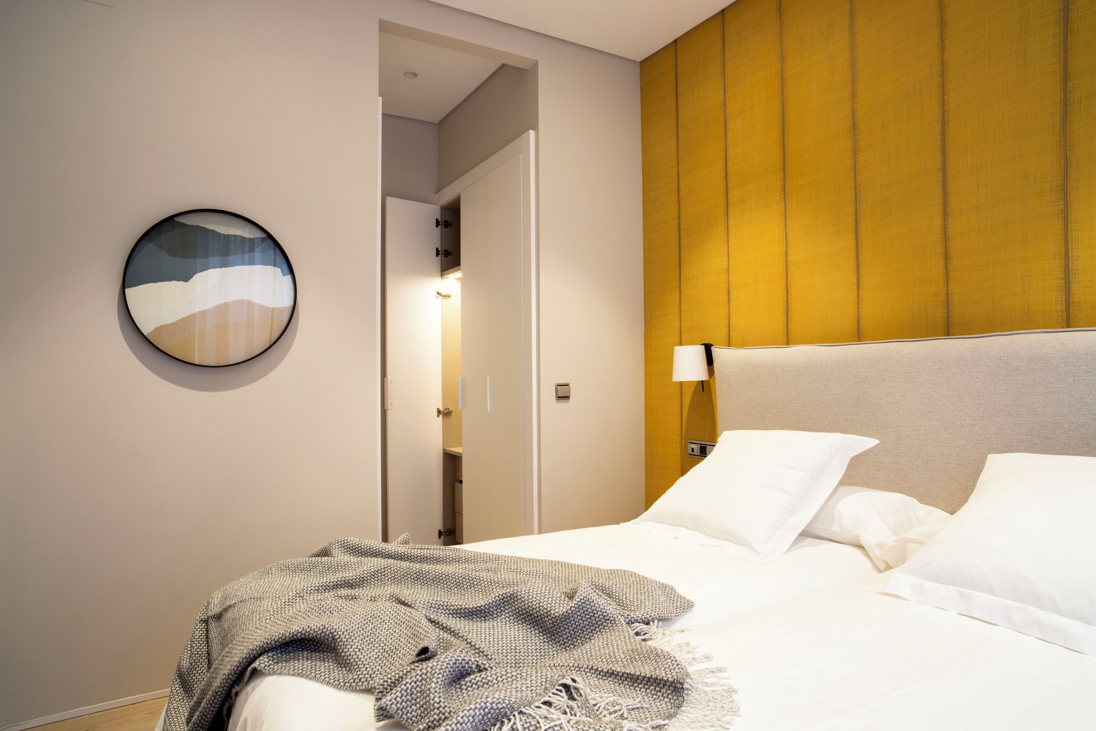 Une chambre d’hôtel avec un lit, une œuvre d’art murale de forme ronde, une lampe de chevet et une porte donnant sur une salle de bain.