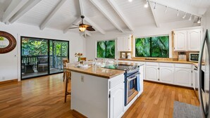 A spacious kitchen with white cabinets, a central island, and a large window overlooking a tropical garden.