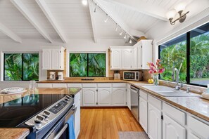 Une cuisine moderne avec des meubles blancs, une cuisinière noire, un four à micro-ondes et une grande fenêtre donnant sur un paysage verdoyant.