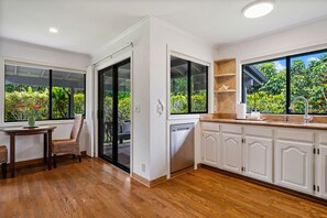 Une cuisine avec des meubles blancs, un plan de travail en bois, un lave-vaisselle encastré et une fenêtre donnant sur un espace verdoyant.