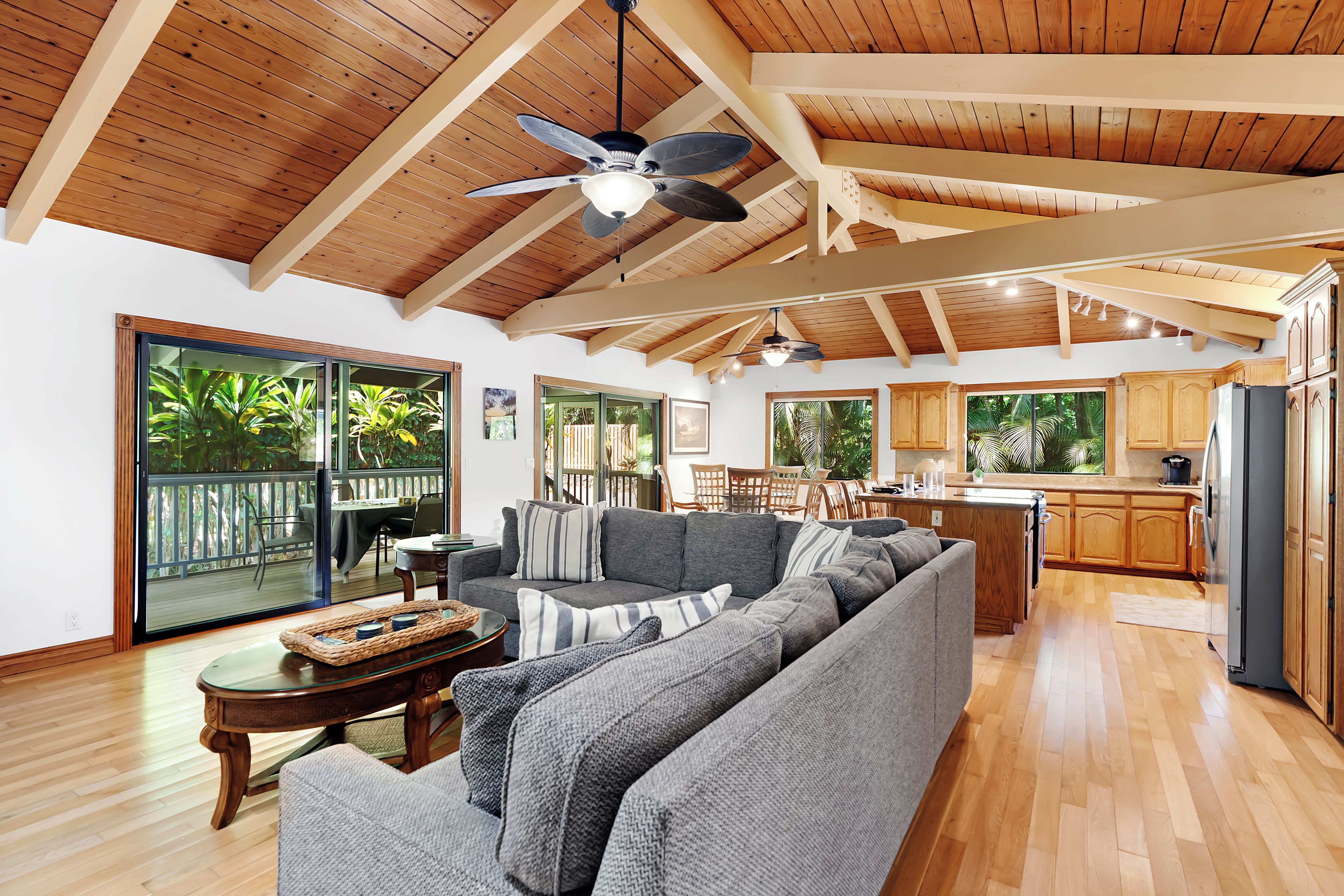 A spacious living area with a large gray sectional sofa, wooden flooring, and a ceiling fan.