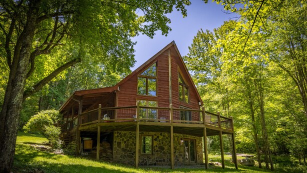 A cabin with a stone foundation, a wooden deck, and a large window. - Base Camp - Cozy Cabin, Close to Snowshoe! (Pocahontas County)