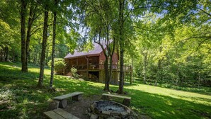A rustic cabin with a deck, surrounded by a forest. There are picnic tables and a fire pit. - Base Camp - Cozy Cabin, Close to Snowshoe! (Pocahontas County)