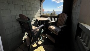 Un espacio de estar al aire libre cubierto con sillas Adirondack y una pequeña mesa, con vistas a un paisaje montañoso.