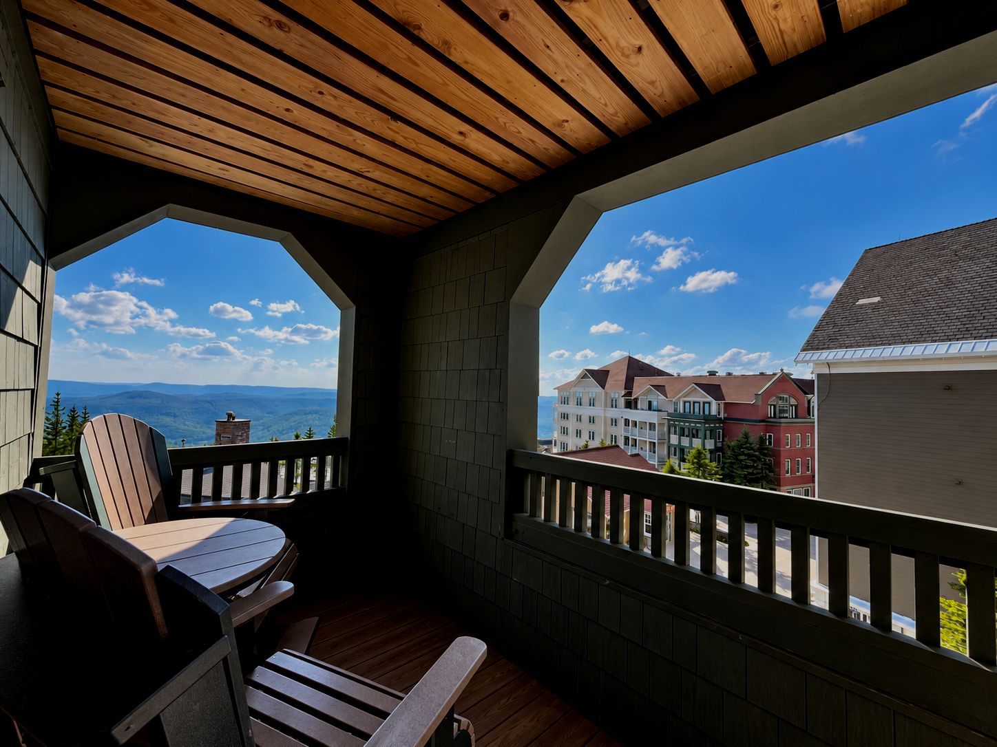 A balcony with wooden flooring and a view of a mountain range and buildings.
