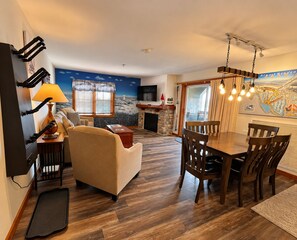 A modern living room with a sofa, dining table, and chairs. There is a fireplace, a TV mounted on the wall, and a map on the wall. - Highland House 302 - Ski-In/Ski-Out! (Snowshoe)