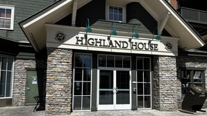 Exterior de Highland House, con fachada de piedra, puertas de cristal amplias y un cartel sobre la entrada.