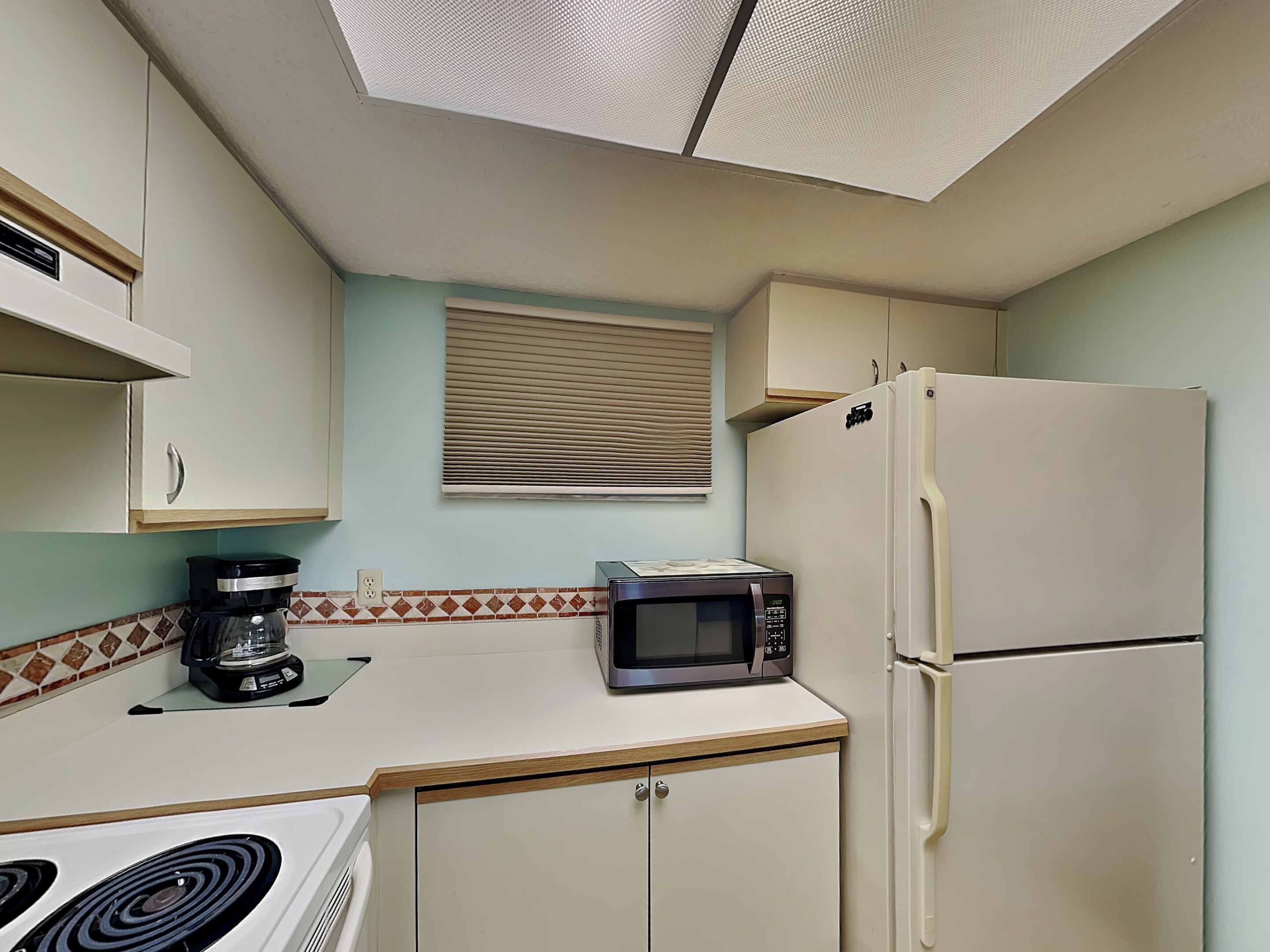 A compact kitchen with a microwave, stove, refrigerator, and a coffee maker.