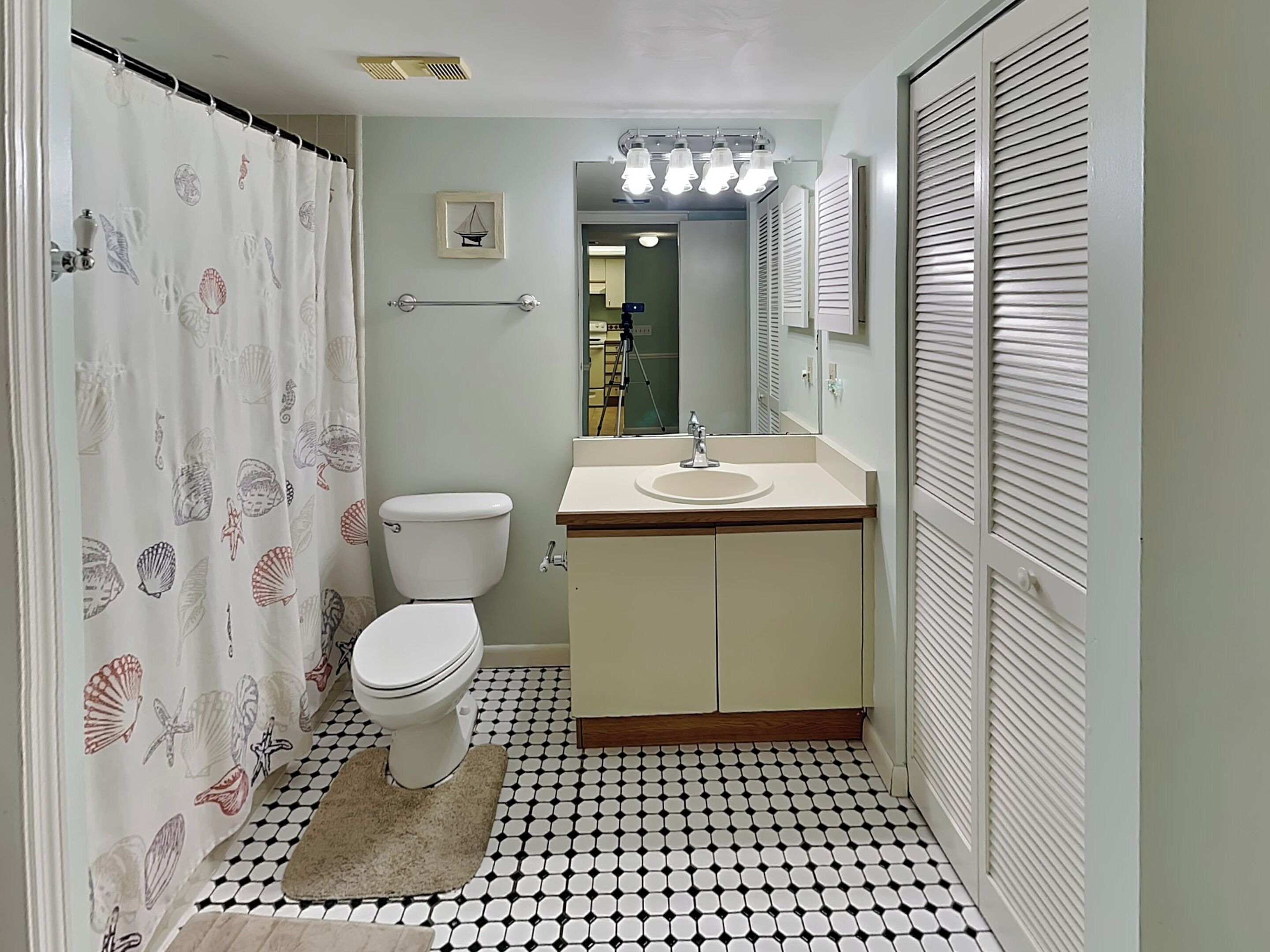A bathroom with a toilet, sink, and shower curtain with a sea shell pattern.