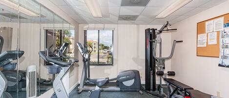 A gym with treadmills, elliptical machines, a bench press, and a wall-mounted mirror.