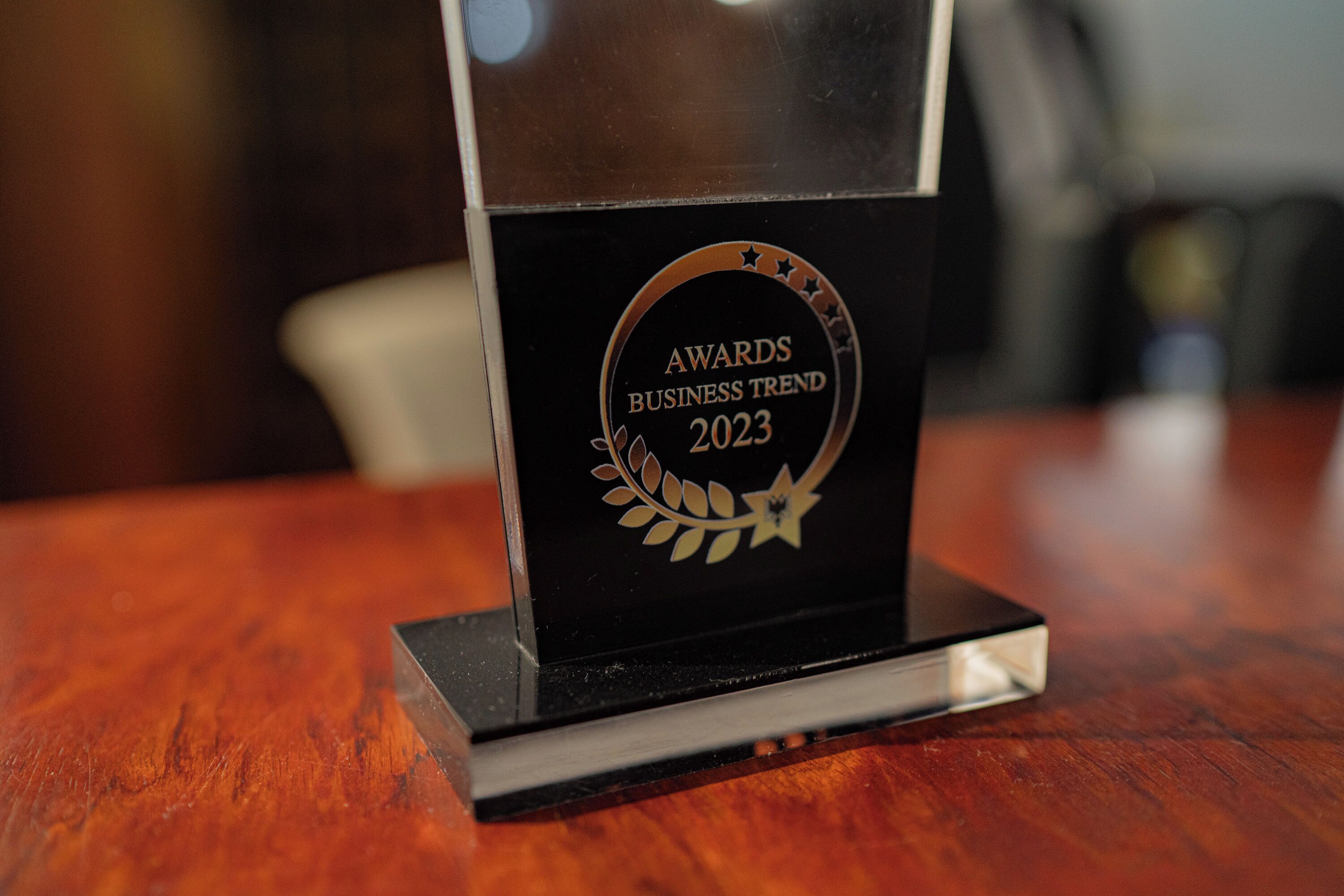 A black award plaque with the text "AWARDS BUSINESS TREND 2023" on a wooden table.