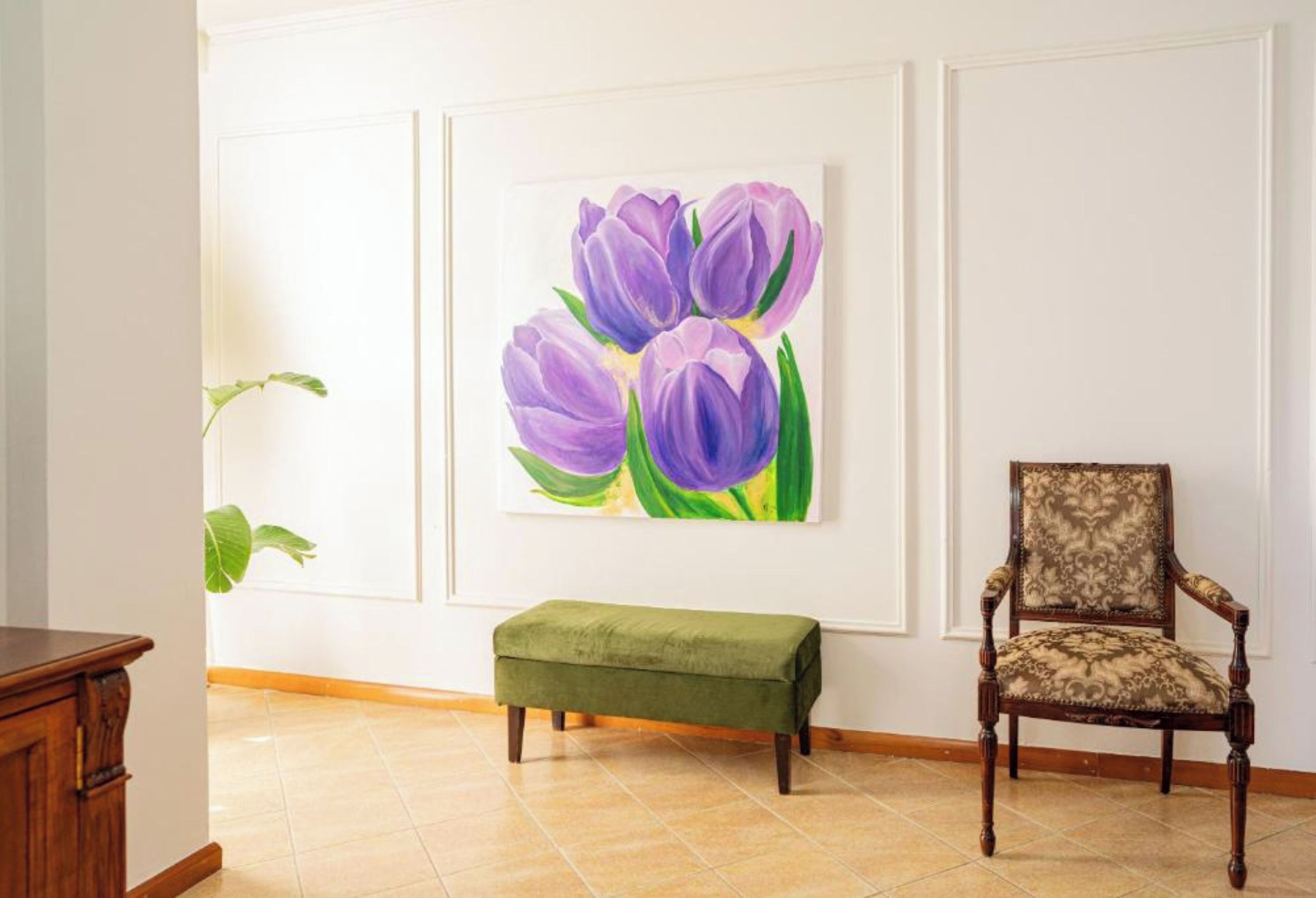 Una habitación con un banco verde, una silla de madera y un cuadro colgado en la pared con flores púrpuras.