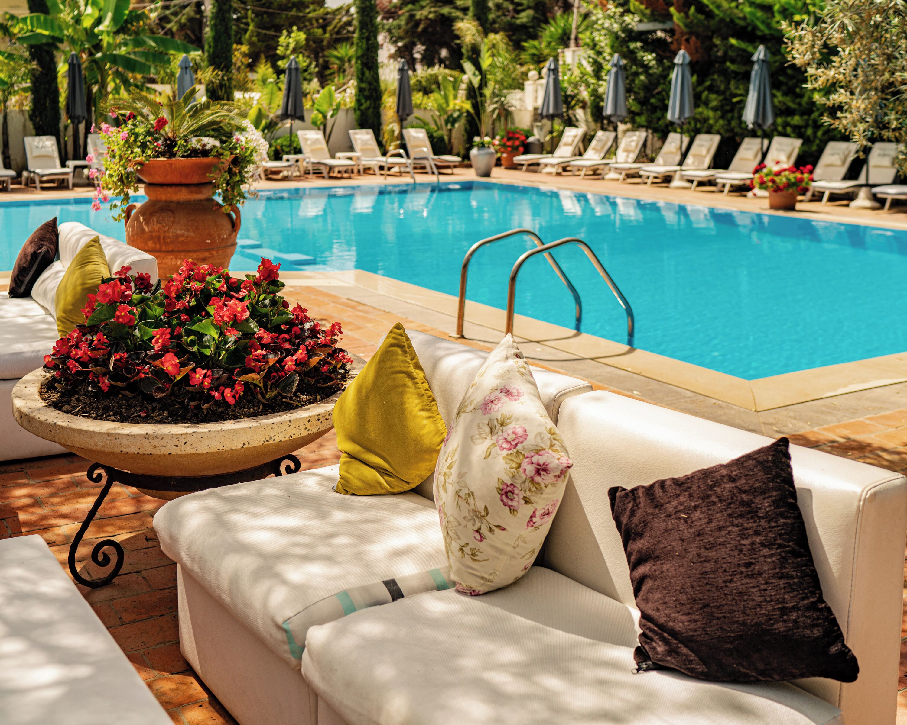 Un espace aménagé au bord de la piscine, avec un canapé blanc, un grand pot de fleurs et des chaises longues.