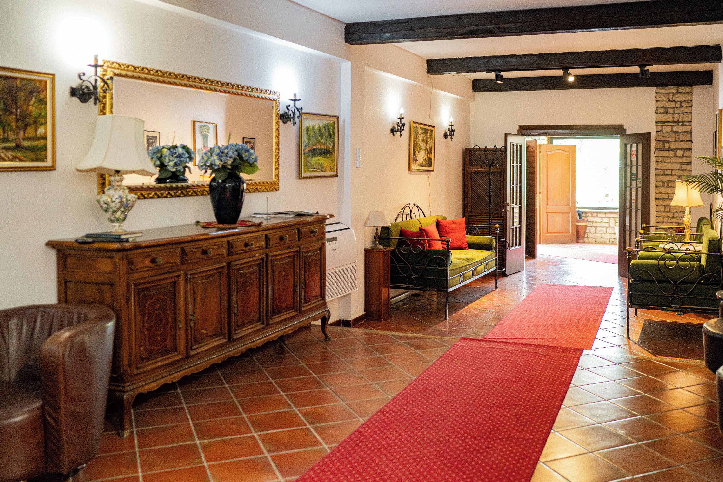 A spacious living area with a wooden cabinet, a sofa, a red rug, and a green armchair.