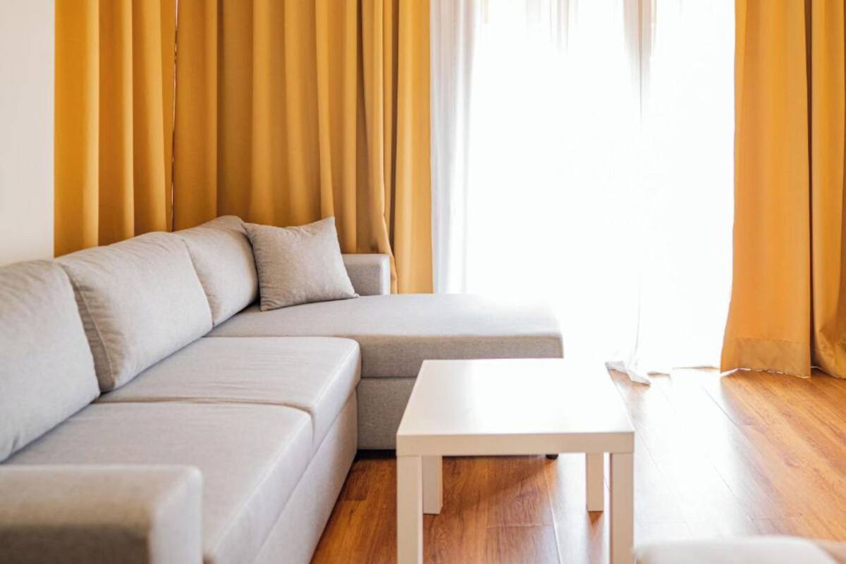 A modern living room with a sectional sofa, a small white table, and yellow curtains.