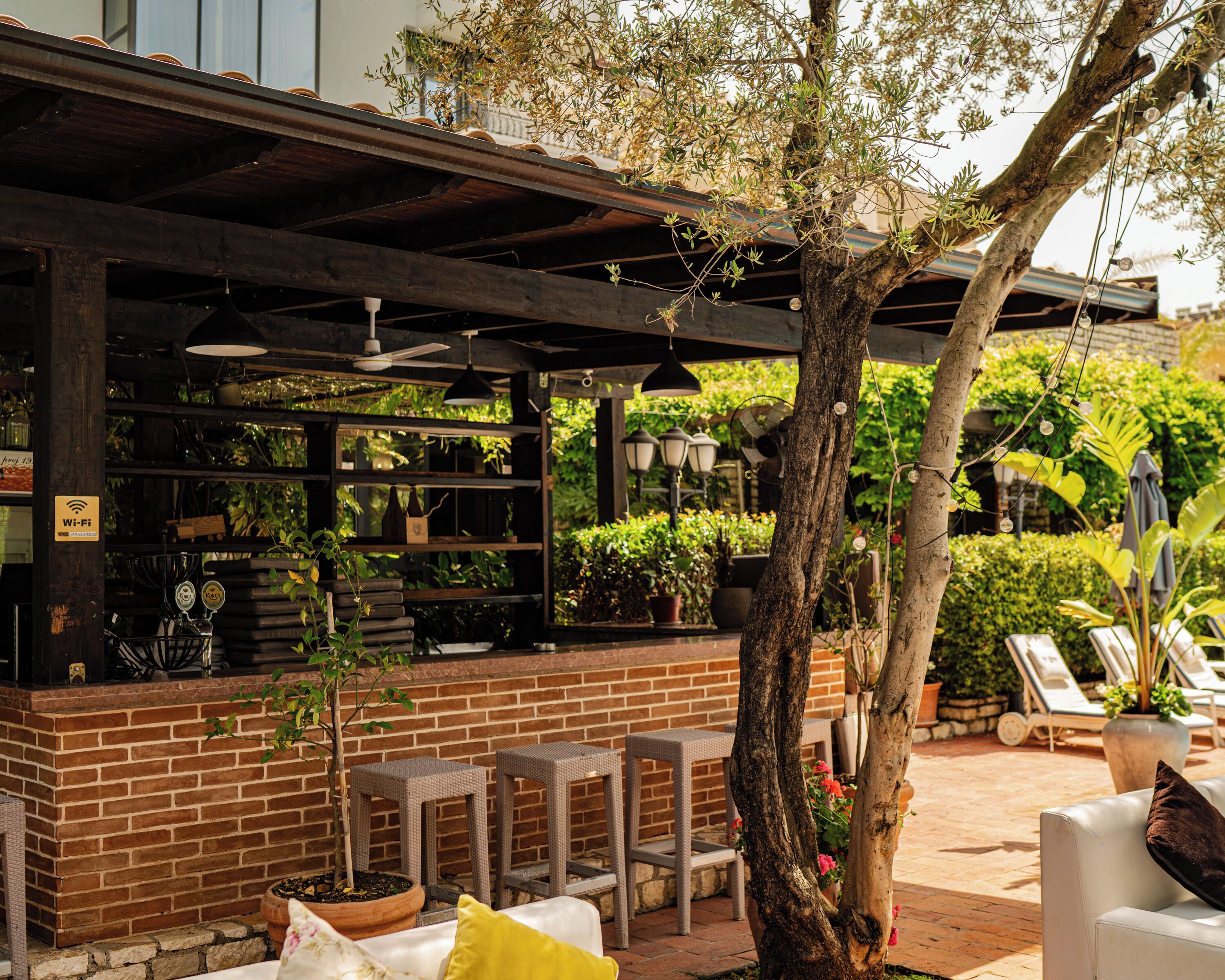 An outdoor bar area with a brick wall, wooden shelves, wicker bar stools, and potted plants.
