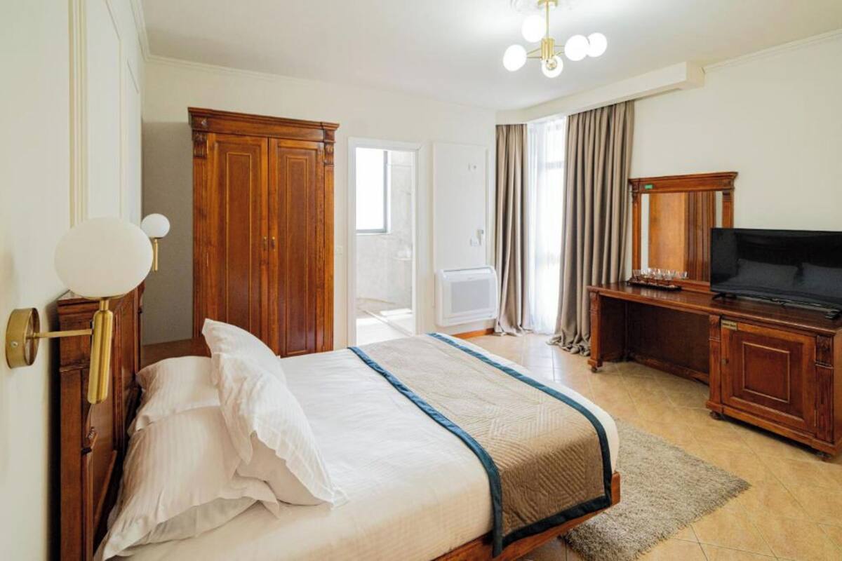 A hotel room with a bed, a television, a wooden wardrobe, and a desk.