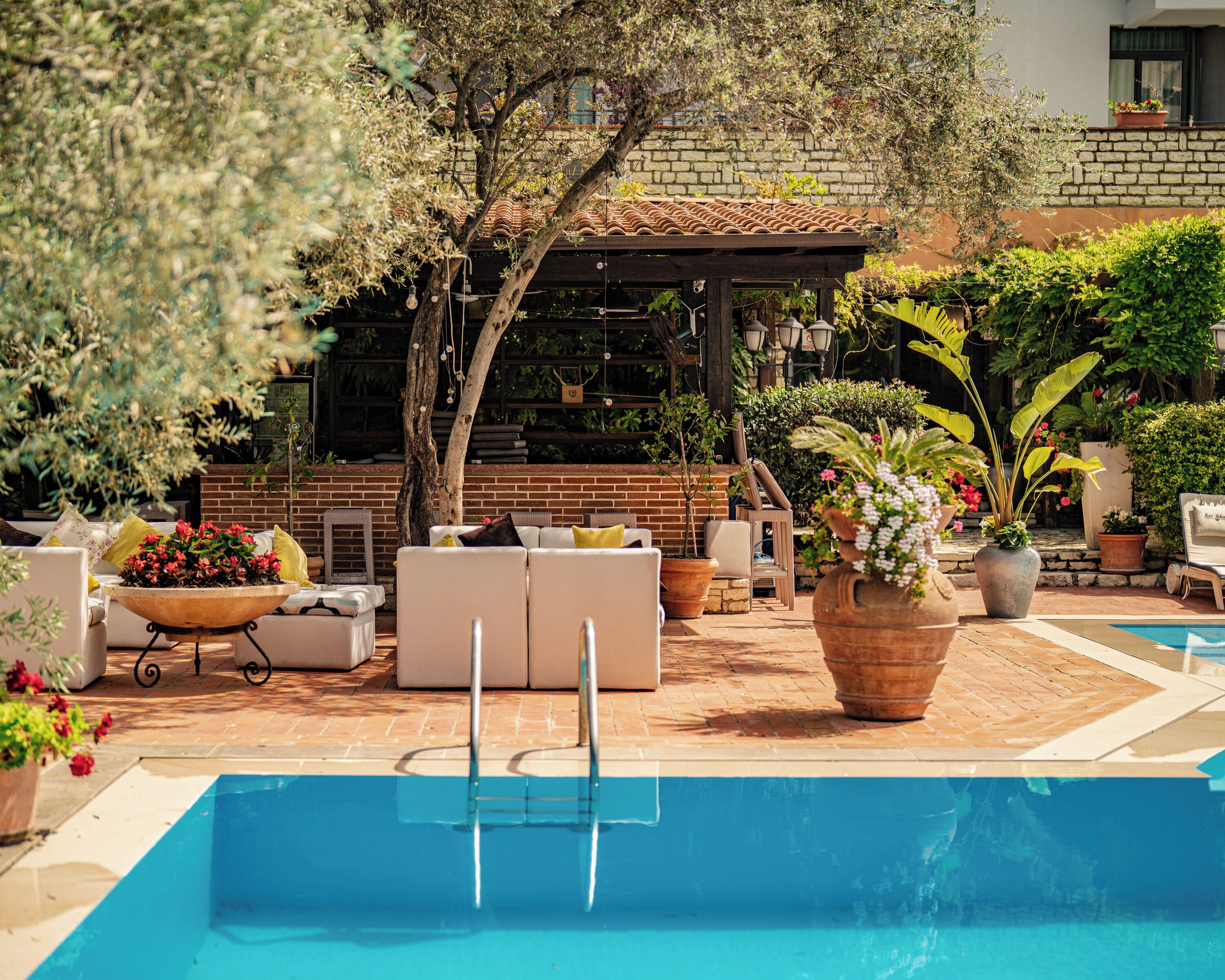 A pool area with a lounge chair, a table with flowers, and a brick wall in the background.