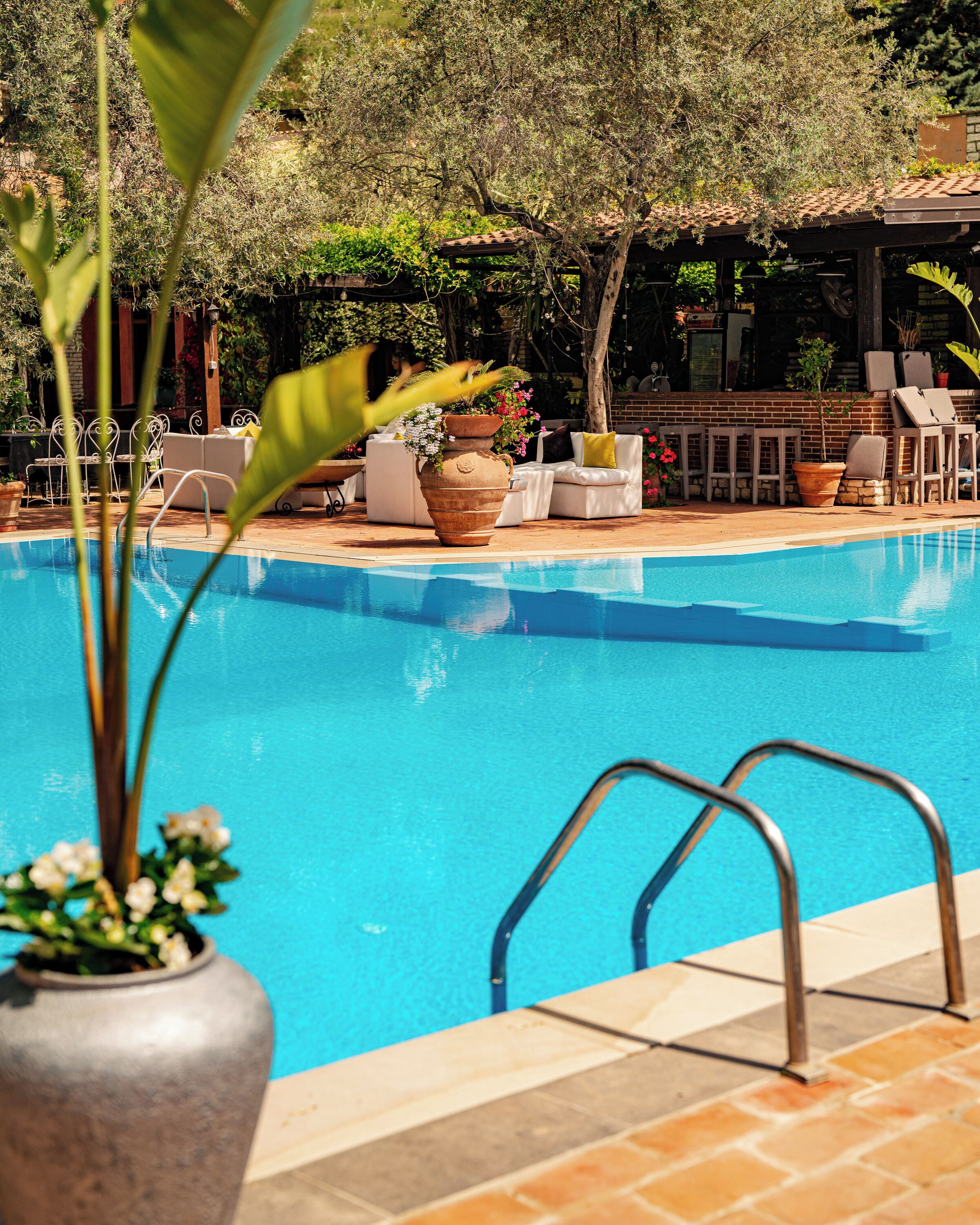 Una piscina con superficie de agua cristalina y azul, rodeada por un suelo de baldosas y mobiliario de exterior.