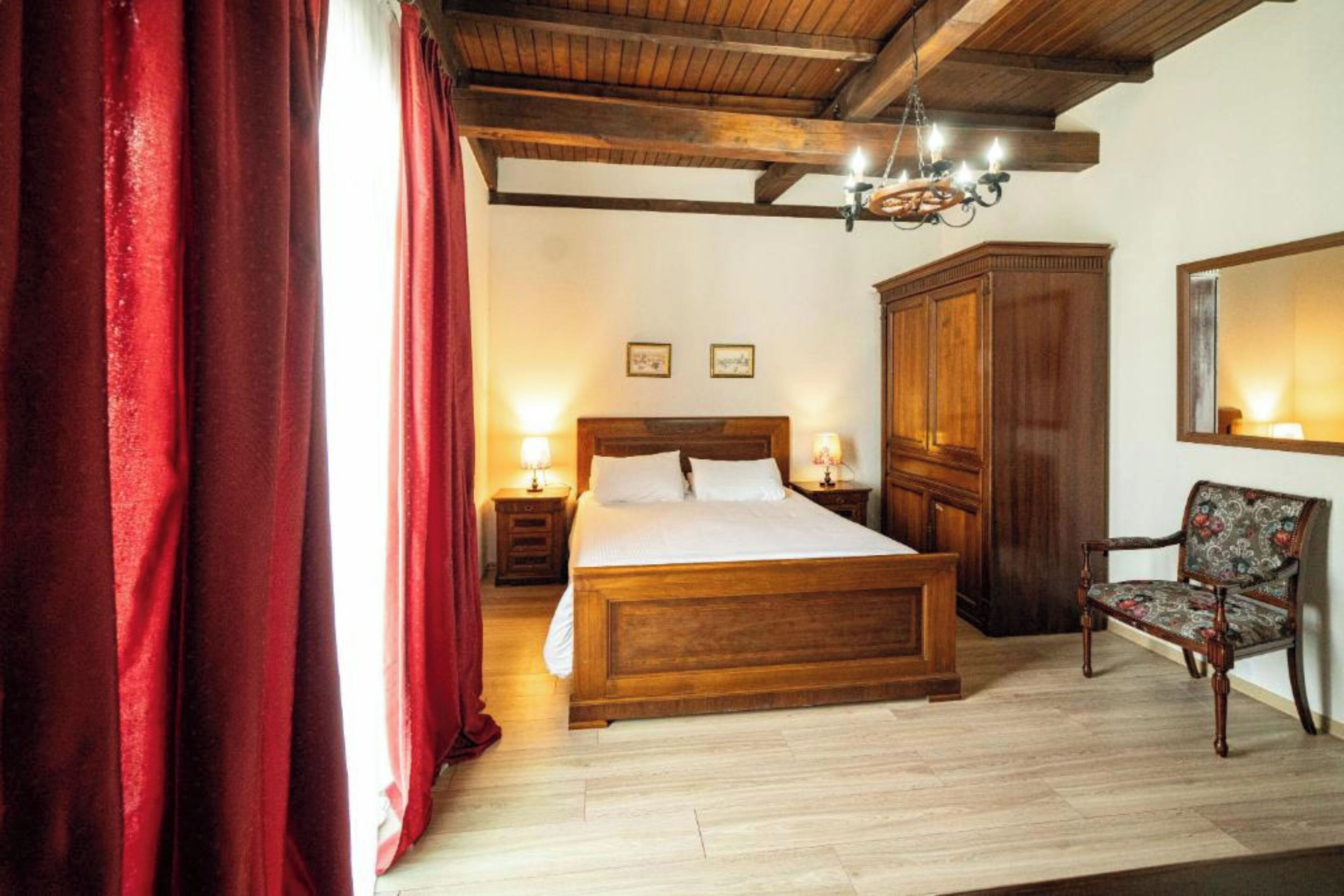 A bedroom with a wooden bed, a nightstand with a lamp, a wardrobe, and a chair.