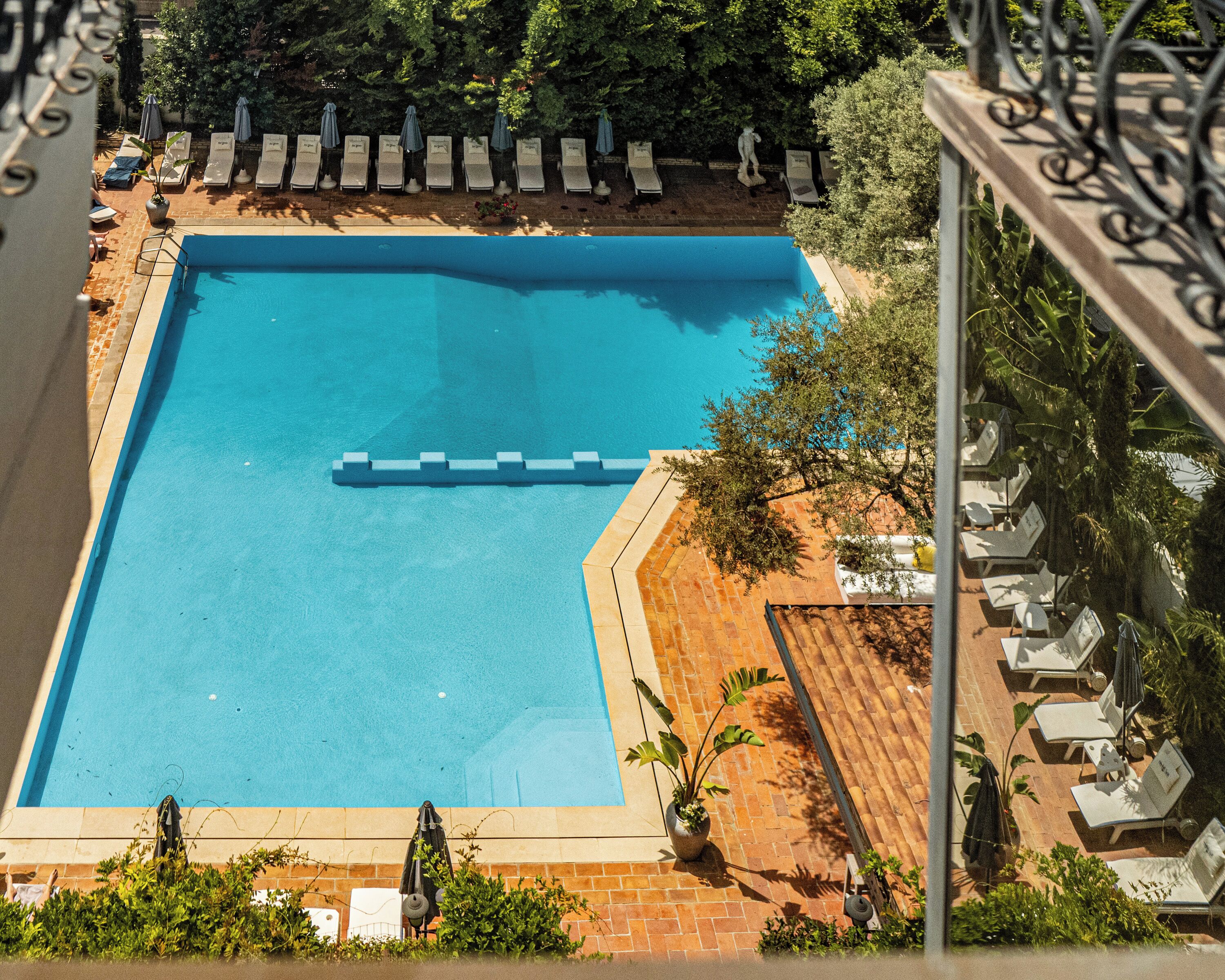 A rectangular swimming pool with a blue interior, surrounded by lounge chairs and umbrellas, and bordered by a brick patio.