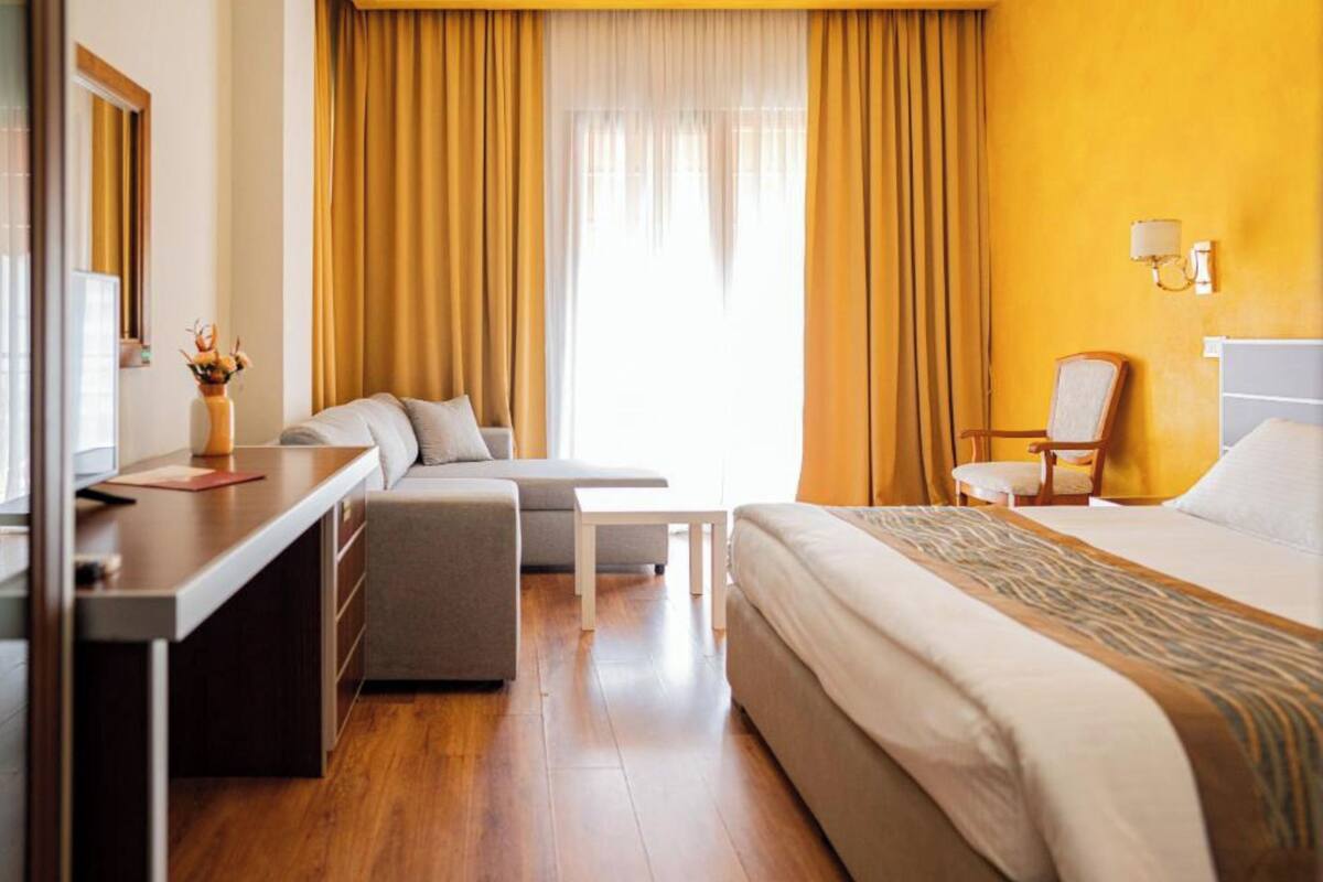 A hotel room with a bed, a desk, a chair, a sofa, and a small table.