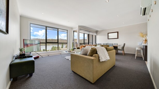 A modern living room with a large window, a sofa, a dining area, and a small bar. - Jasper 4 in the Town Centre with Lake views (Jindabyne)
